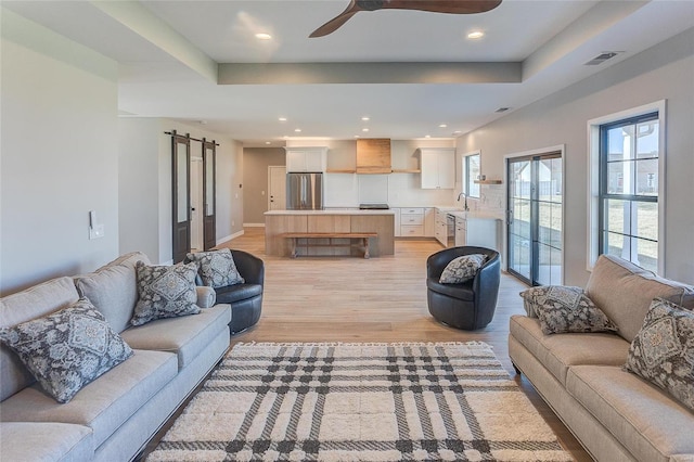 living room with a barn door, a raised ceiling, a ceiling fan, and light wood-style floors