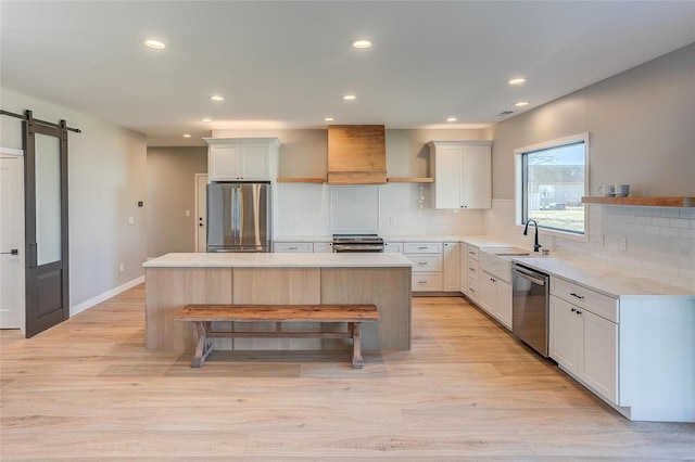 kitchen with a barn door, appliances with stainless steel finishes, a kitchen island, a sink, and wall chimney exhaust hood