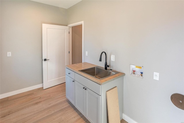 washroom featuring light wood finished floors, hookup for a washing machine, cabinet space, a sink, and baseboards