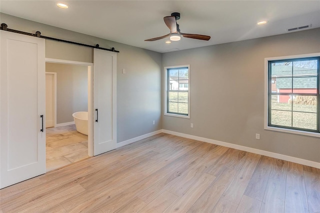 unfurnished bedroom with light wood-type flooring, baseboards, and a barn door