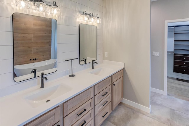 bathroom featuring double vanity, a soaking tub, baseboards, and a sink