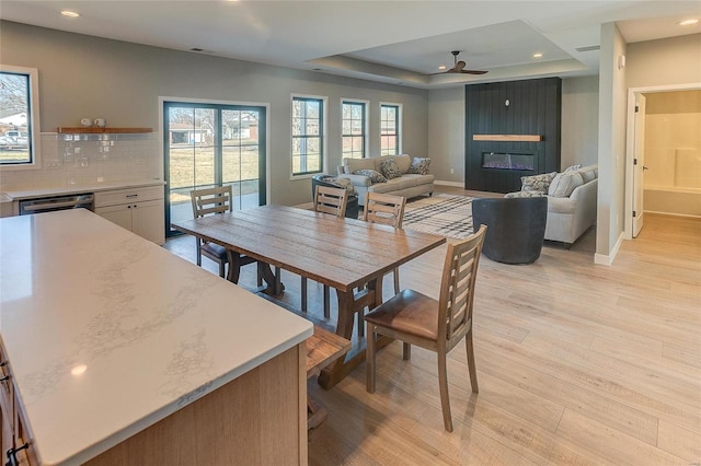 dining space featuring a large fireplace, baseboards, a raised ceiling, and light wood-style floors