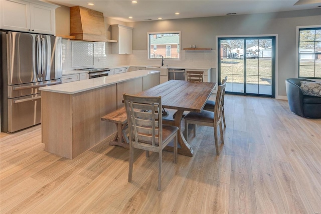 kitchen with wall chimney exhaust hood, appliances with stainless steel finishes, light wood-type flooring, and tasteful backsplash