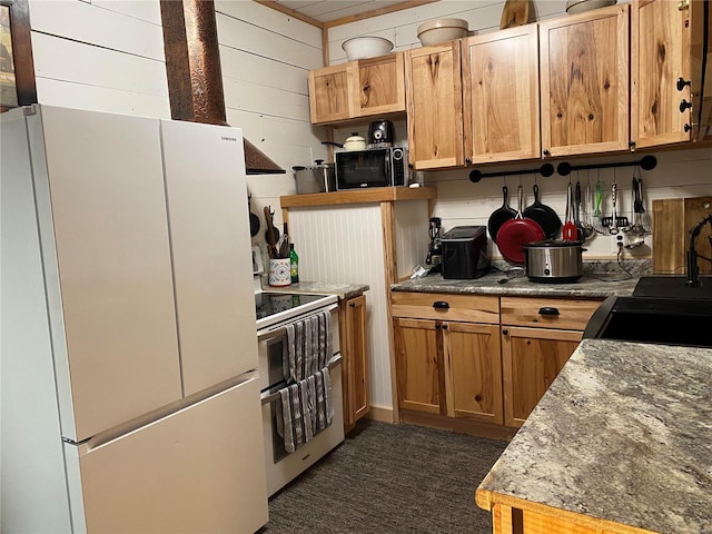 kitchen with wooden walls, freestanding refrigerator, double oven range, black microwave, and a sink