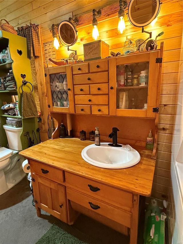 bathroom with wooden walls, toilet, and vanity