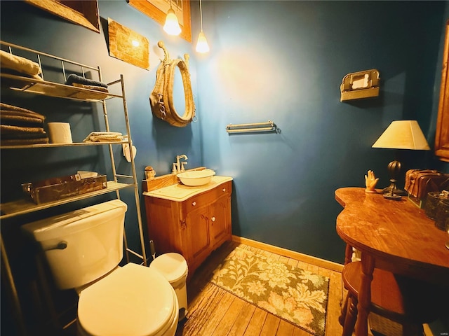 half bath with baseboards, vanity, toilet, and wood finished floors