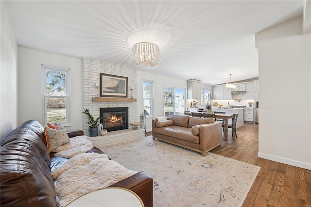 living room with a notable chandelier, a fireplace, baseboards, and wood-type flooring