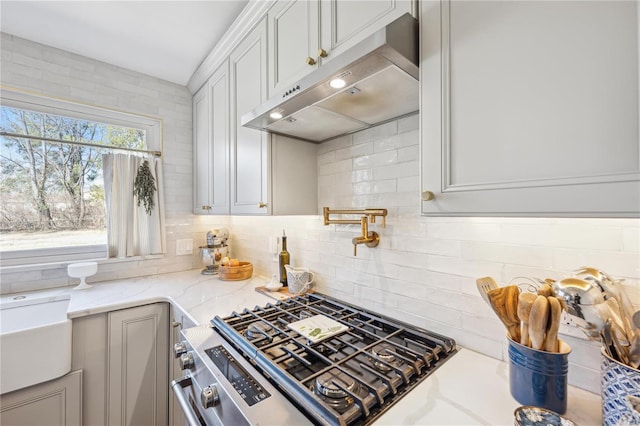 kitchen featuring stainless steel gas stove, under cabinet range hood, light stone counters, white cabinets, and decorative backsplash