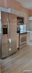 kitchen featuring light wood finished floors, white cabinetry, appliances with stainless steel finishes, and extractor fan