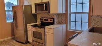 kitchen featuring light countertops, light wood-style flooring, appliances with stainless steel finishes, white cabinets, and baseboards