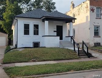 view of front facade with an outbuilding, a front lawn, a detached garage, and covered porch