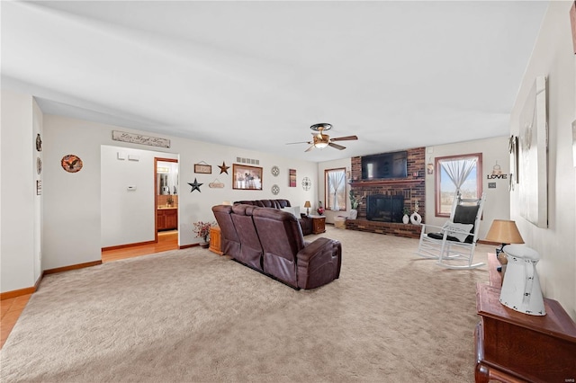 living room featuring light colored carpet, a brick fireplace, baseboards, and ceiling fan