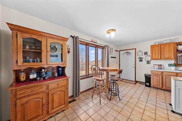 interior space with backsplash, glass insert cabinets, baseboards, light countertops, and light tile patterned flooring