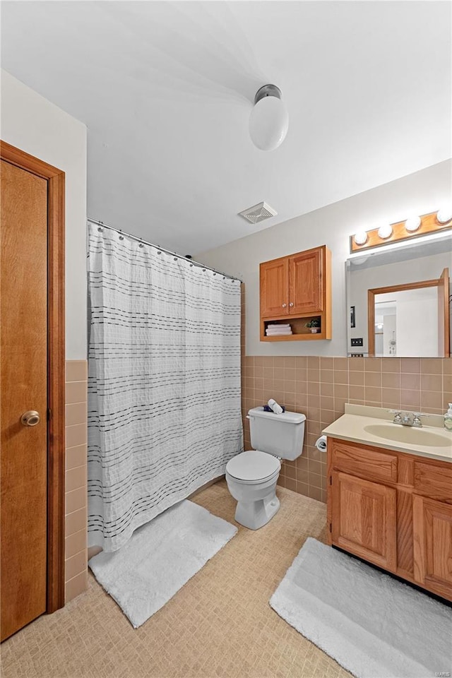 bathroom featuring visible vents, toilet, vanity, wainscoting, and tile walls