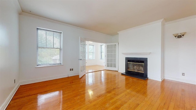 unfurnished living room featuring a glass covered fireplace, light wood-style floors, baseboards, and ornamental molding