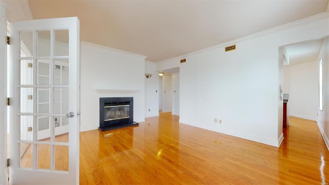 unfurnished living room featuring baseboards, wood finished floors, a glass covered fireplace, and crown molding