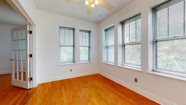 empty room with a wealth of natural light, baseboards, light wood-style flooring, and a ceiling fan