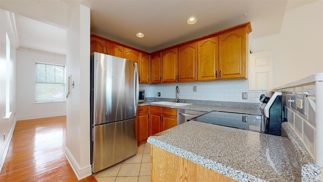 kitchen featuring brown cabinetry, stainless steel appliances, decorative backsplash, and a sink