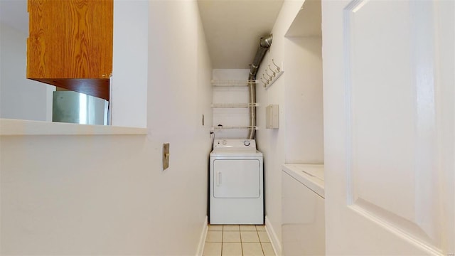 clothes washing area featuring light tile patterned floors, baseboards, and washing machine and clothes dryer