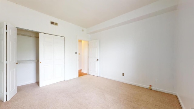 unfurnished bedroom with light colored carpet, visible vents, a closet, and baseboards