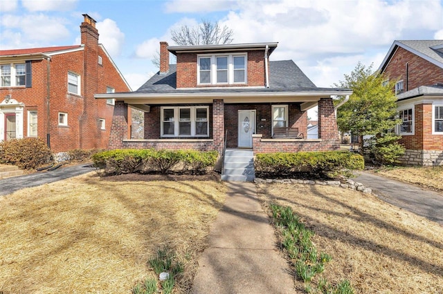 bungalow with a front yard, brick siding, covered porch, and a shingled roof