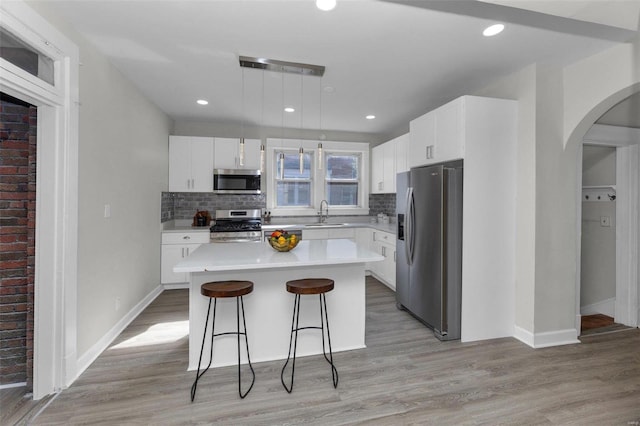 kitchen featuring a center island, stainless steel appliances, arched walkways, light wood-style floors, and decorative backsplash