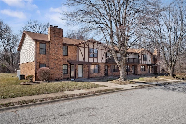 tudor house with a chimney, a front lawn, central AC, and brick siding