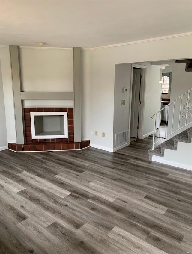 unfurnished living room with a tile fireplace, visible vents, stairway, and wood finished floors