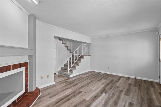 unfurnished living room with baseboards, a tiled fireplace, stairway, ornamental molding, and wood finished floors