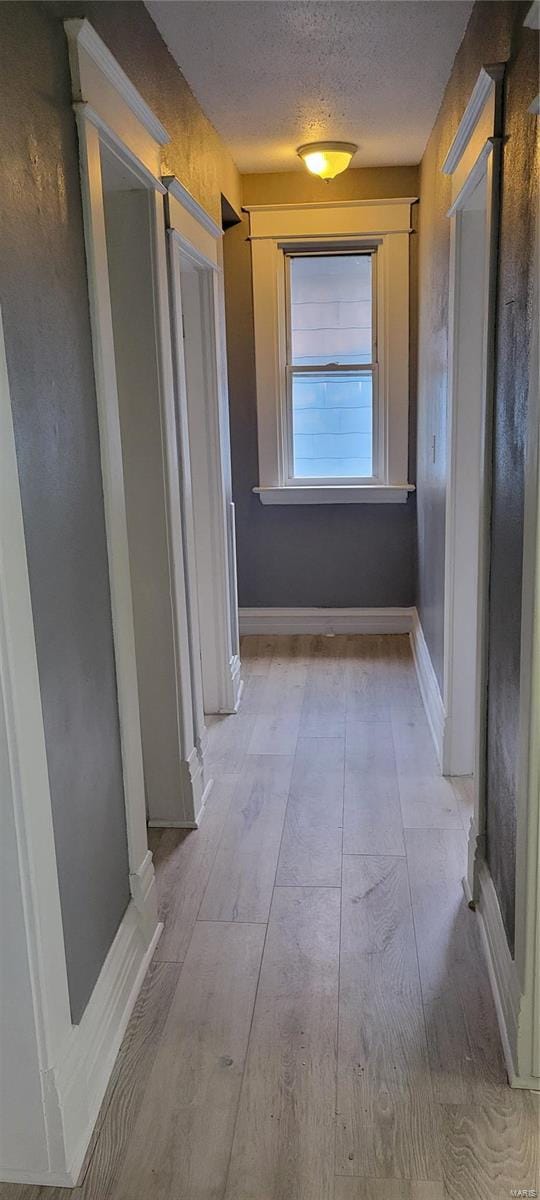 hallway with light wood finished floors, a textured ceiling, and baseboards