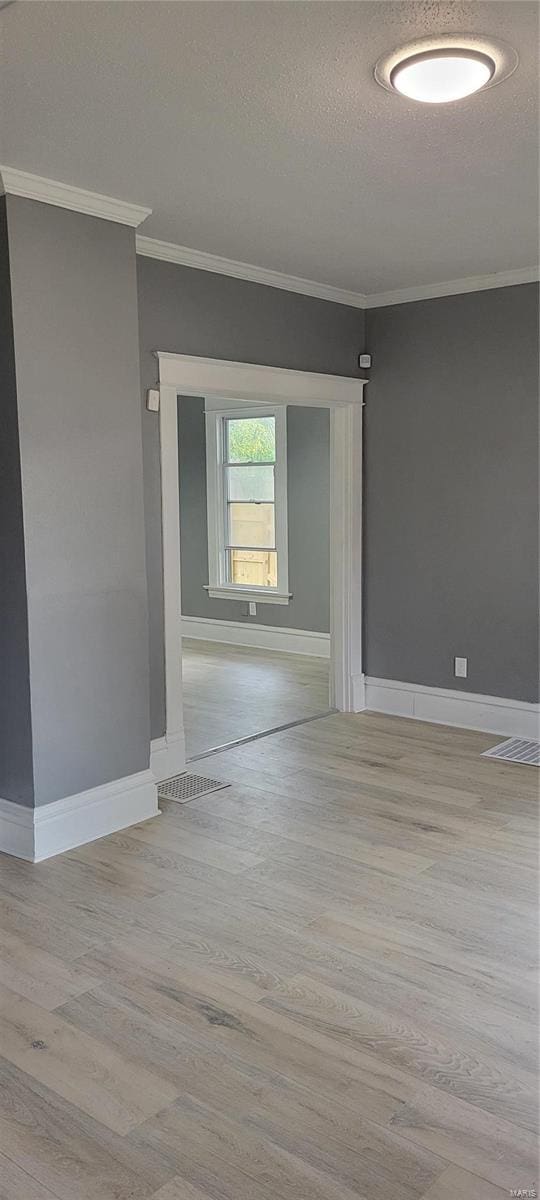 spare room featuring light wood-style flooring, a textured ceiling, baseboards, and crown molding
