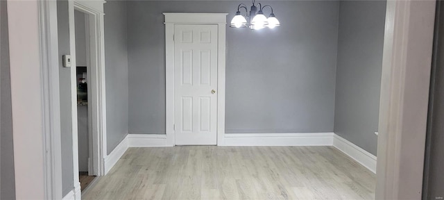 unfurnished dining area featuring baseboards, light wood-type flooring, and an inviting chandelier
