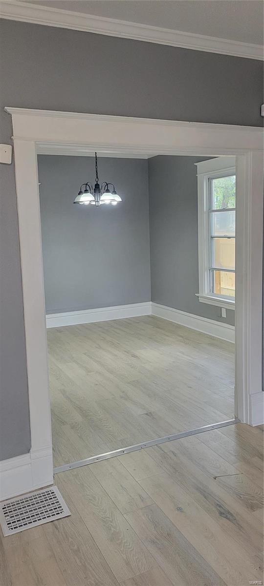 unfurnished dining area with light wood-style floors, an inviting chandelier, baseboards, and ornamental molding
