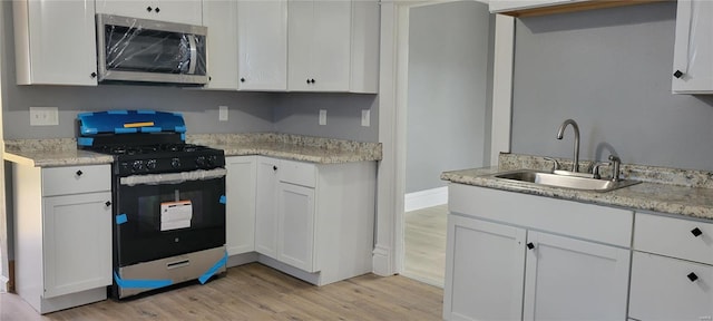 kitchen featuring stainless steel microwave, light wood-style flooring, white cabinets, range with gas cooktop, and a sink