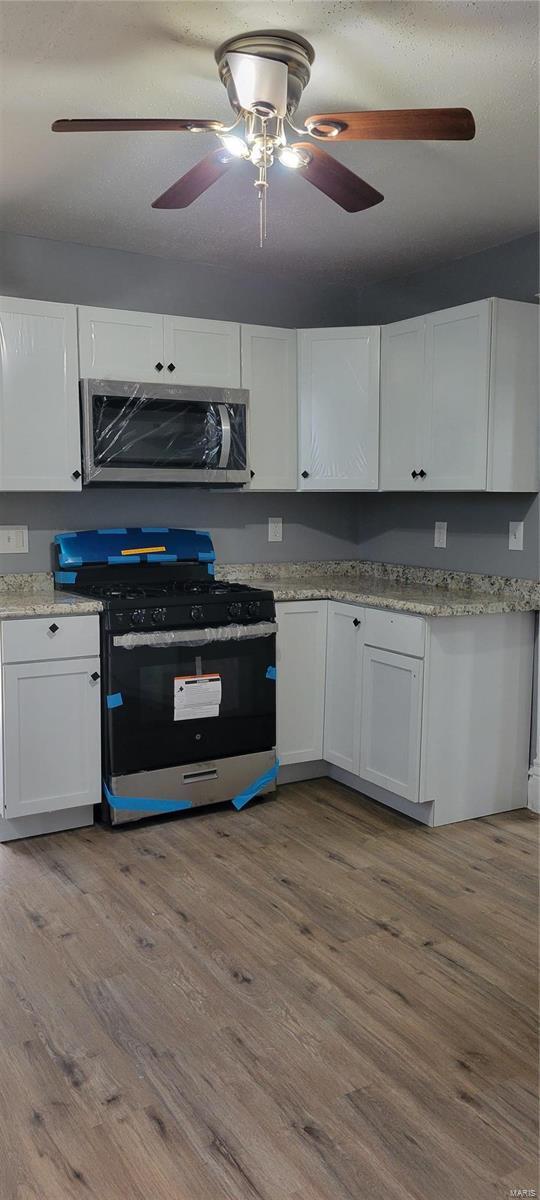 kitchen with a ceiling fan, stainless steel microwave, white cabinetry, gas stove, and wood finished floors