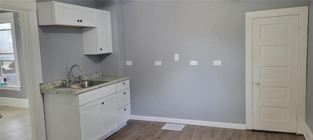 kitchen featuring dark wood-type flooring, white cabinets, a sink, and baseboards