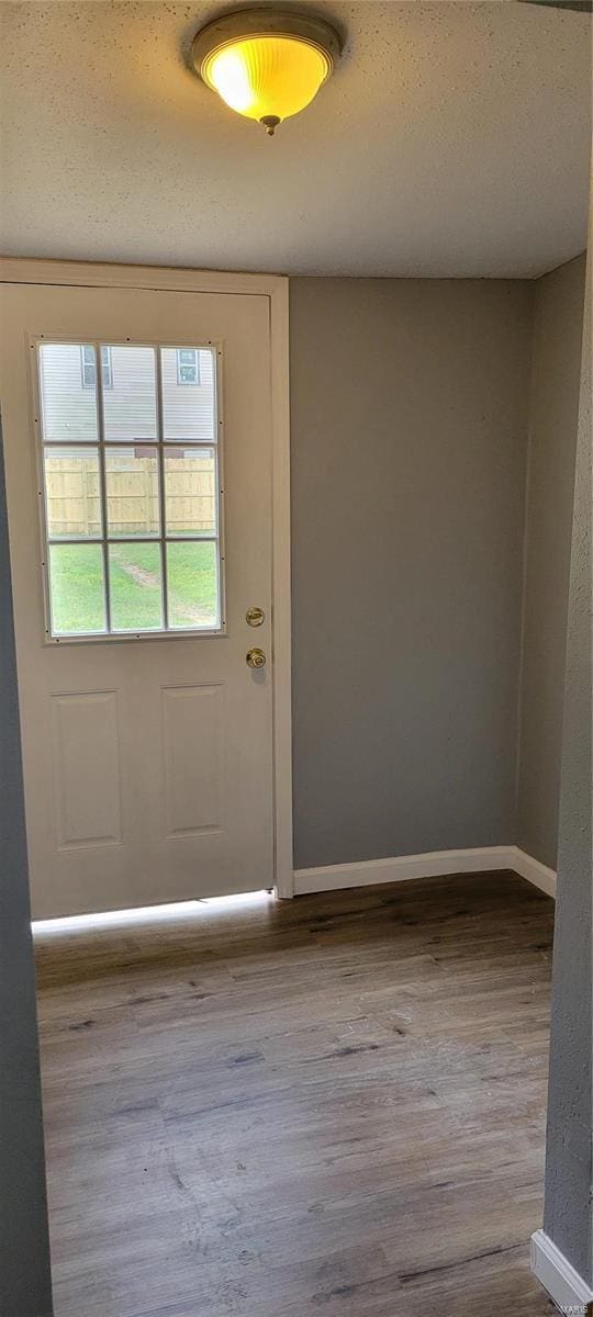 doorway to outside with a textured ceiling, wood finished floors, and baseboards