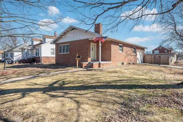 view of side of home with a lawn, fence, a garage, brick siding, and a chimney