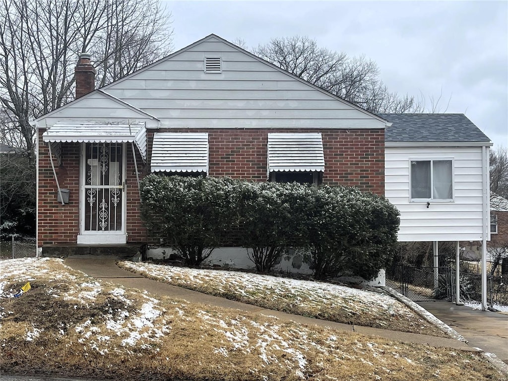 view of front facade with brick siding, a chimney, and roof with shingles