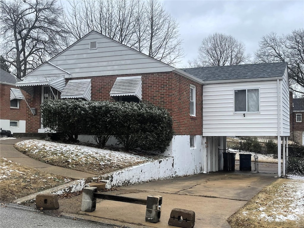 view of side of property with a carport, concrete driveway, brick siding, and roof with shingles