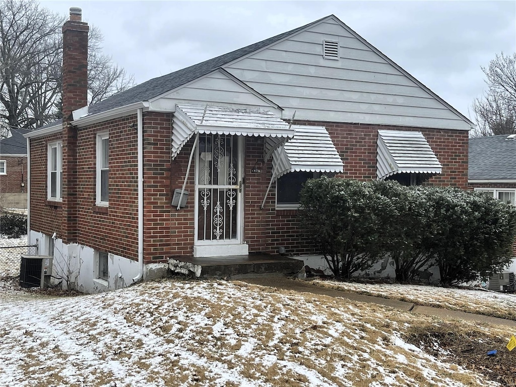 bungalow-style home with cooling unit, brick siding, and a chimney