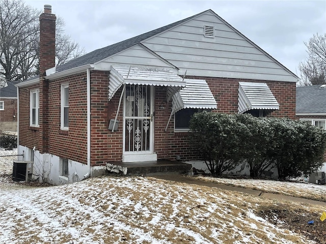 bungalow-style home with cooling unit, brick siding, and a chimney