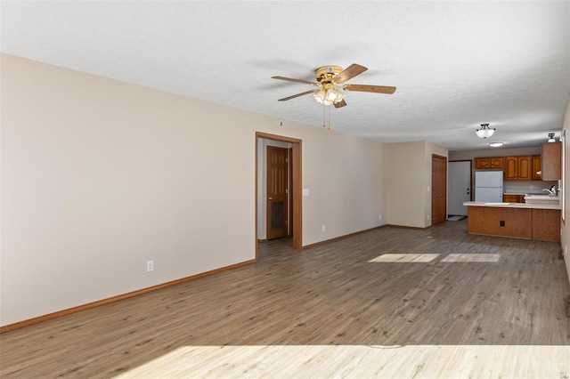 unfurnished living room featuring baseboards, light wood-style flooring, ceiling fan, a textured ceiling, and a sink