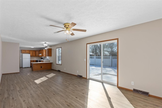 unfurnished living room featuring a ceiling fan, a textured ceiling, visible vents, and wood finished floors