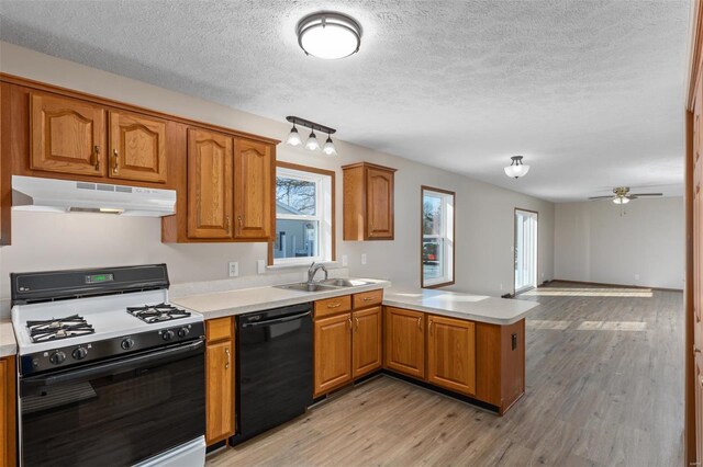 kitchen featuring under cabinet range hood, a peninsula, a sink, range with gas stovetop, and black dishwasher