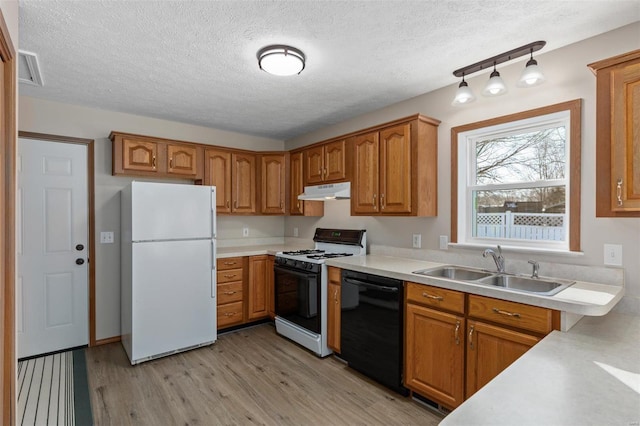 kitchen with black dishwasher, freestanding refrigerator, a sink, gas range, and under cabinet range hood