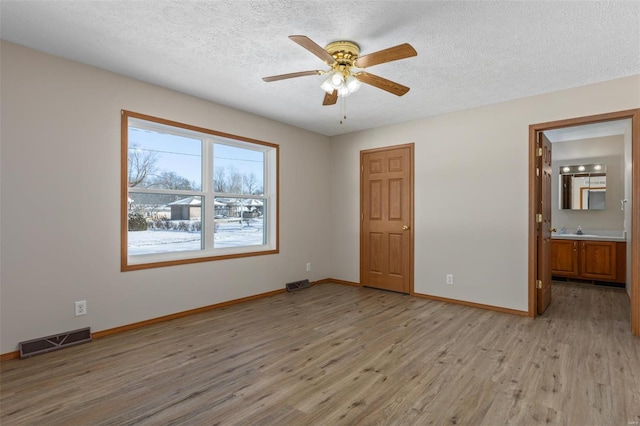 empty room featuring light wood-style flooring, a sink, visible vents, and baseboards