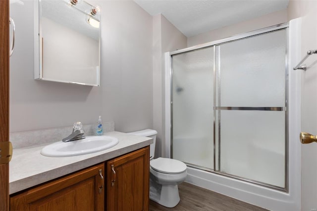 bathroom featuring toilet, wood finished floors, a textured ceiling, vanity, and a shower stall