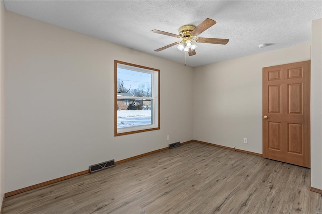 spare room with light wood-style floors, baseboards, visible vents, and a textured ceiling