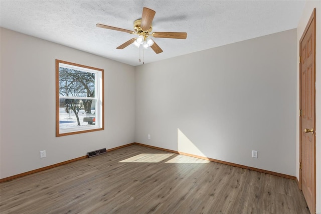 empty room featuring a textured ceiling, visible vents, baseboards, a ceiling fan, and light wood finished floors